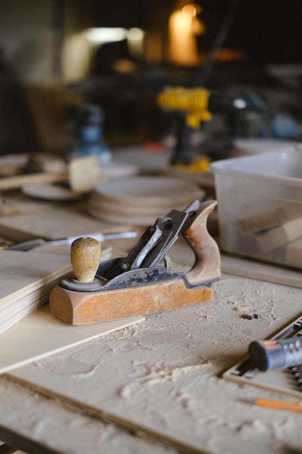 A hand plane resting on a bench with a candle glowing softly behind